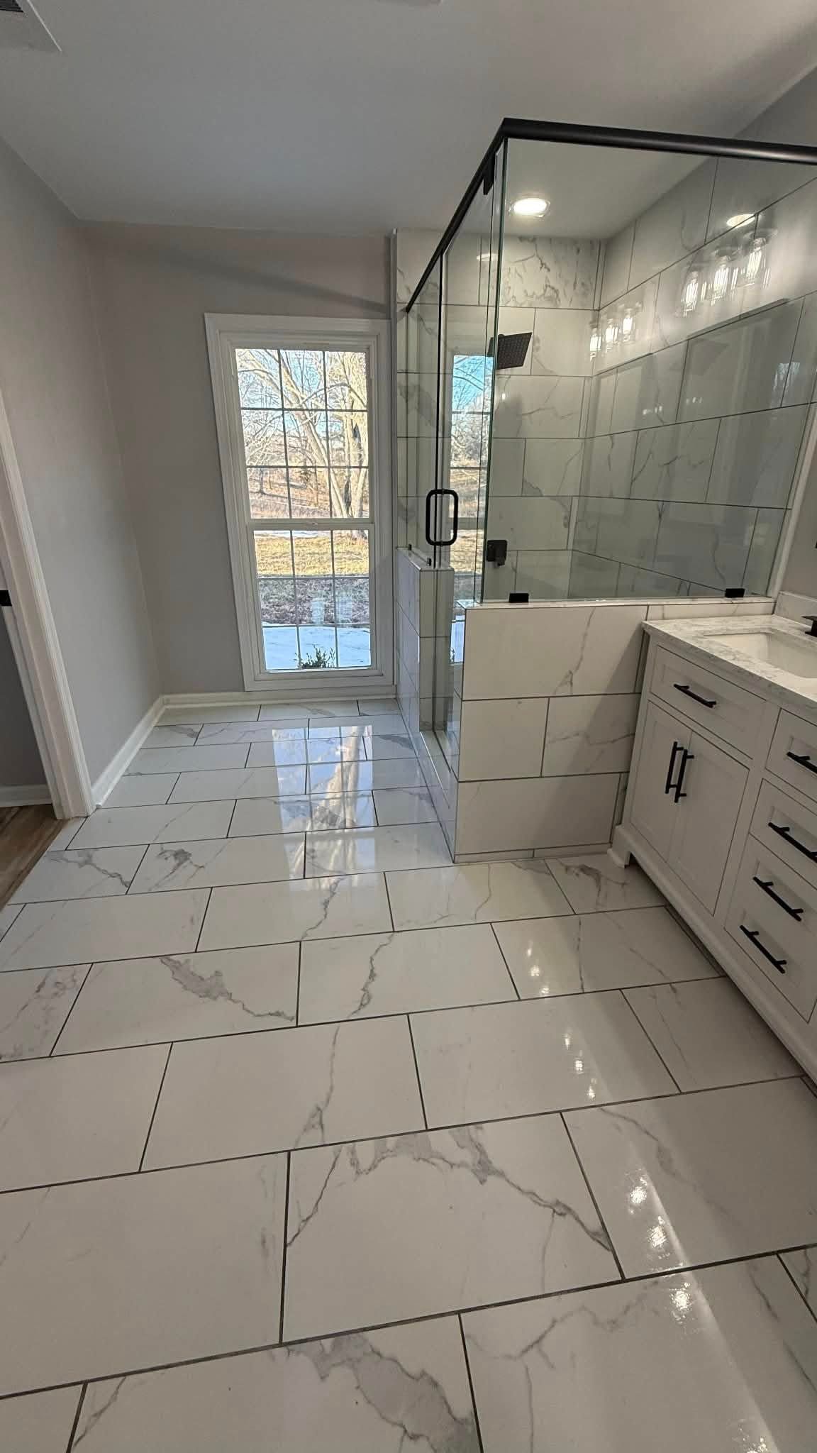 Bright modern bathroom with large mirror, white cabinets, and a glass shower enclosure.