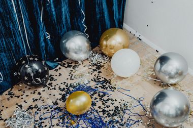 Silver, gold, and white balloons scattered on a confetti-covered floor beside a blue backdrop.