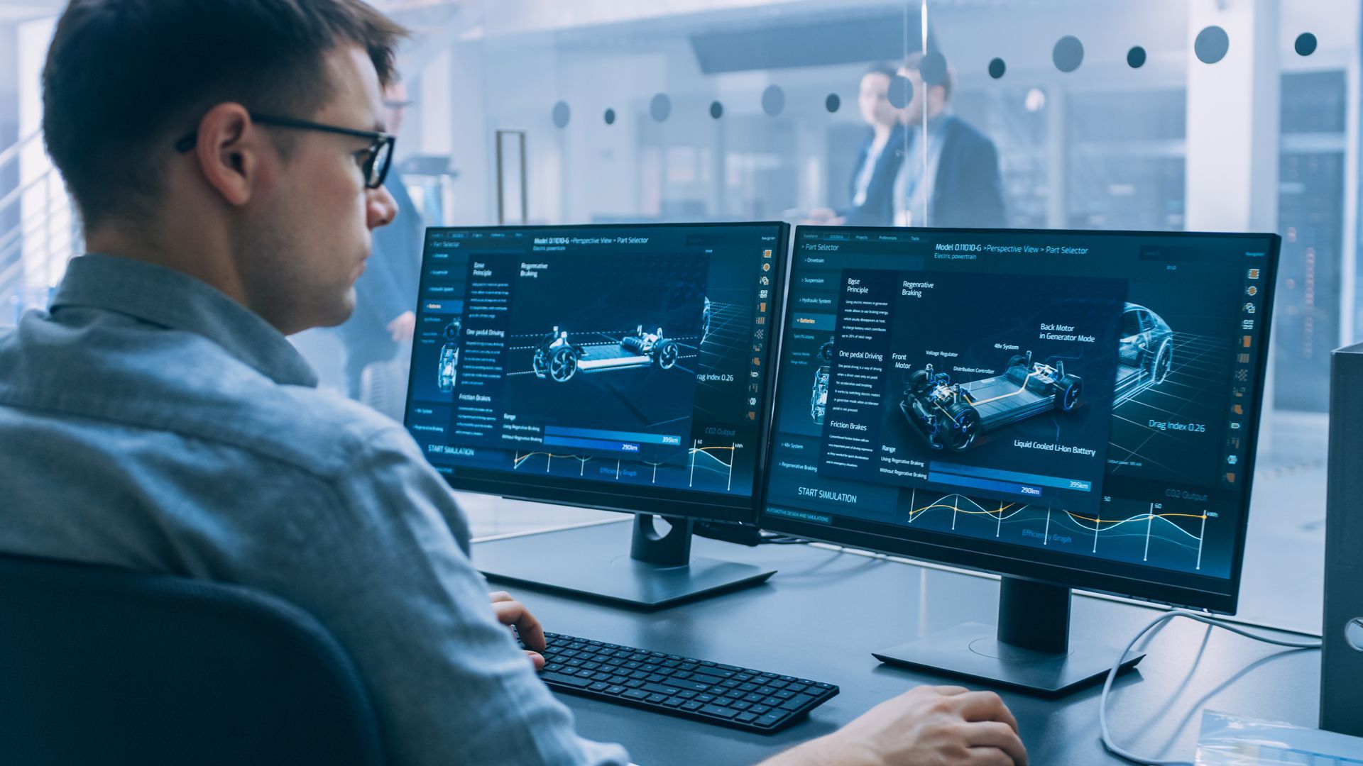 Man using computer, looking at dual monitors displaying vehicle schematics in a modern office.
