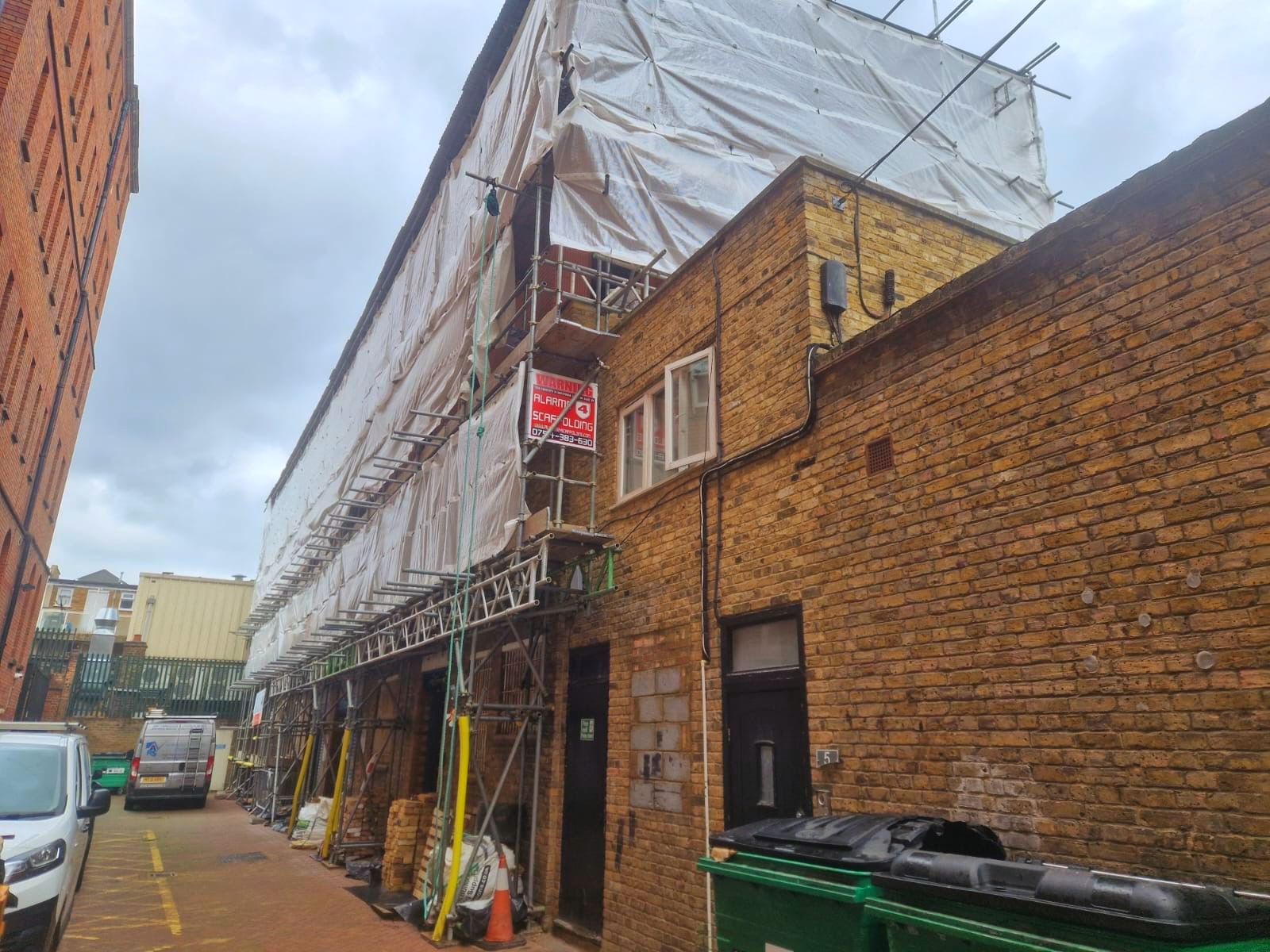 A brick building with scaffolding and a trash can in front of it.