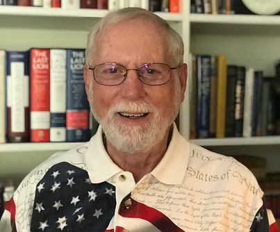 Smiling man in glasses and patriotic shirt seated before bookshelves