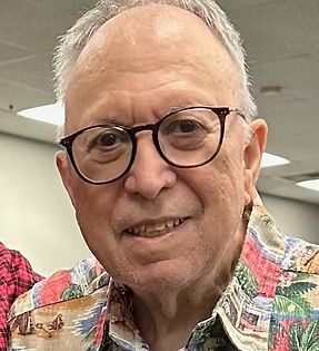 Smiling man wearing round glasses and a colorful patterned shirt indoors