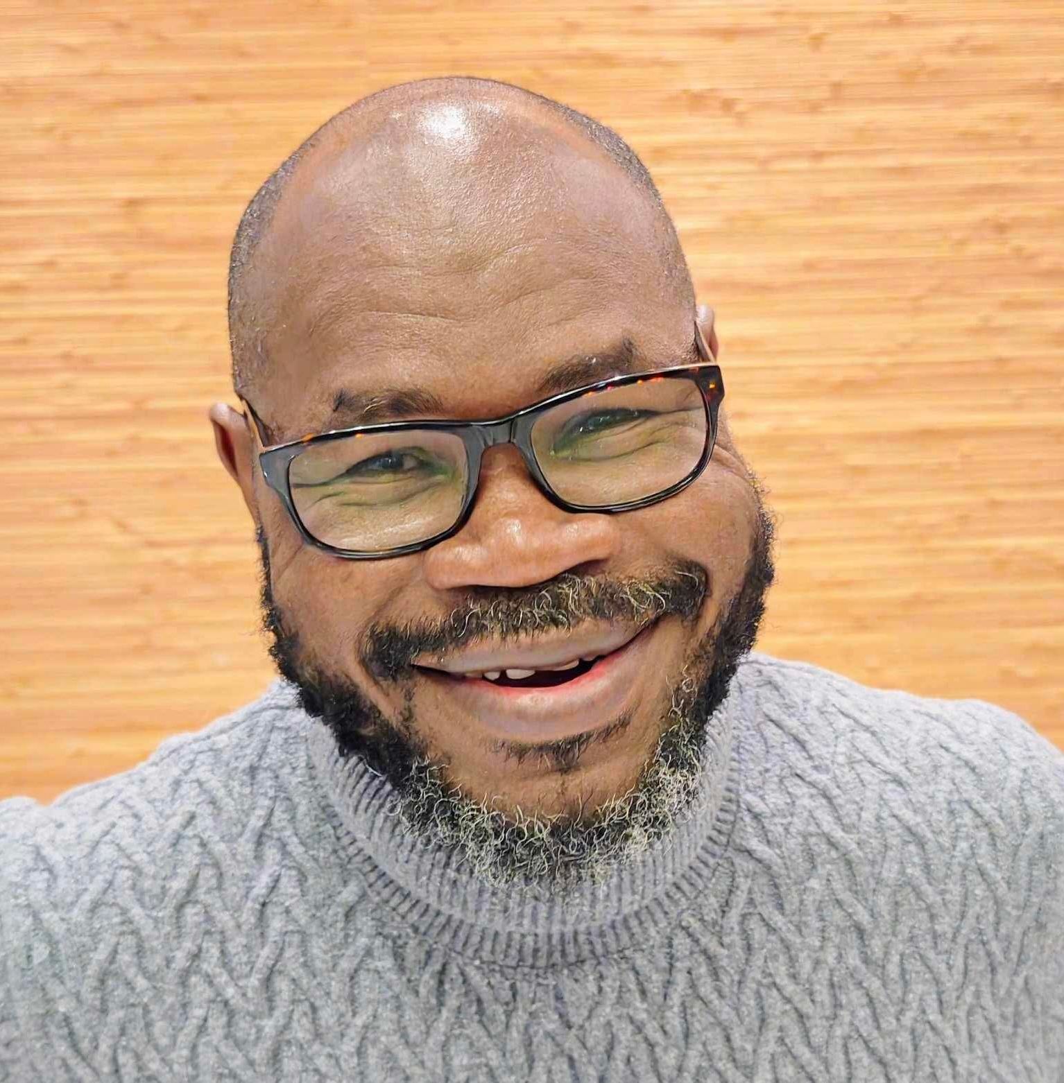 Man wearing glasses and a gray sweater smiles, looking toward the viewer.