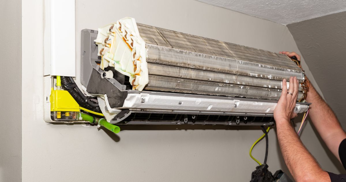 A man is cleaning an air conditioner on a wall.