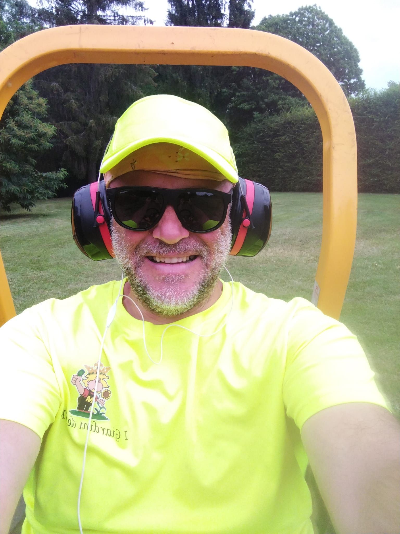 Persona con maglietta e berretto giallo fluo, occhiali da sole e paraorecchie, che si scatta un selfie all'aperto.