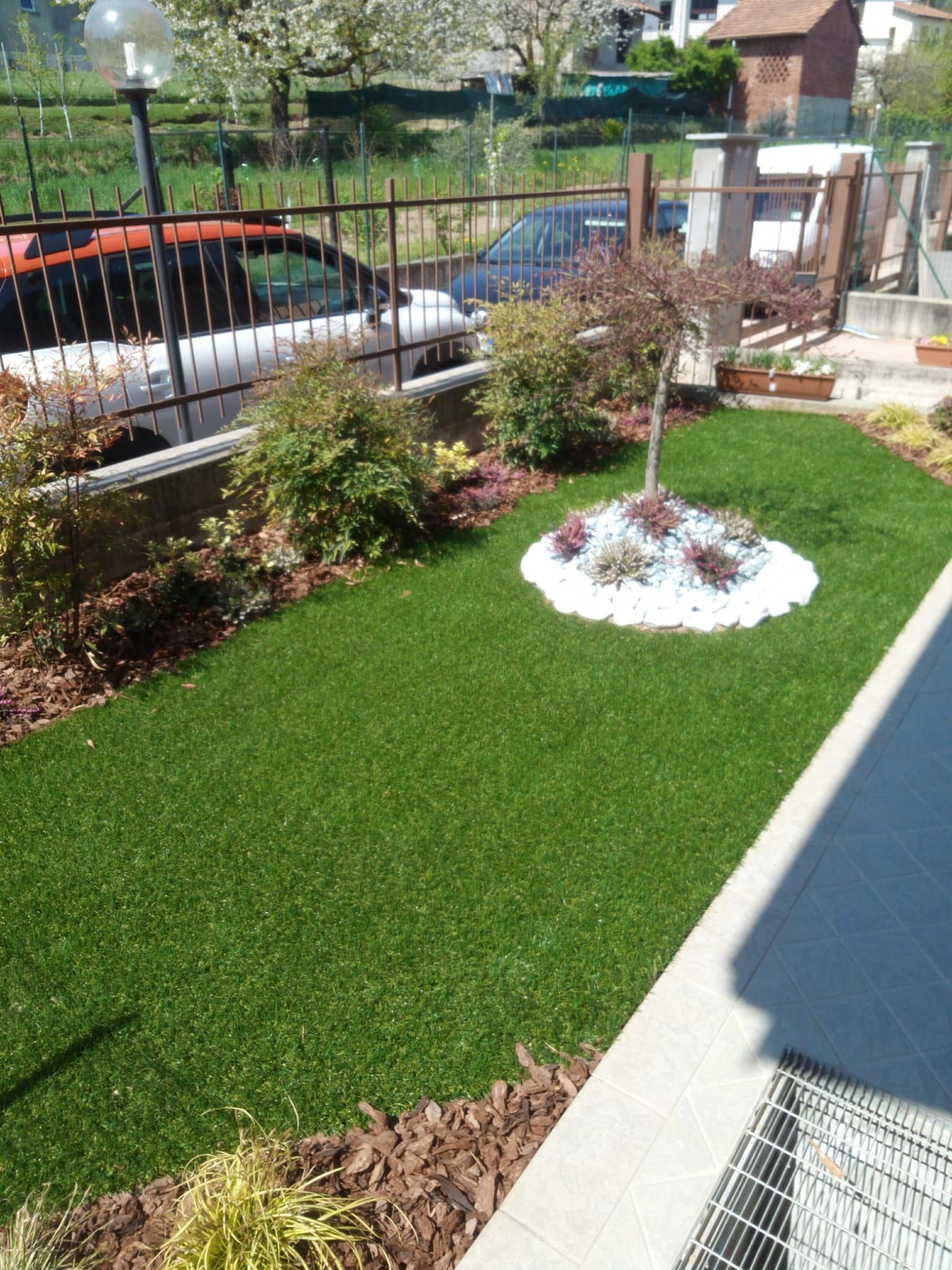 Giardino anteriore curato con erba artificiale, aiuola e recinzione in metallo nero accanto a un vialetto.