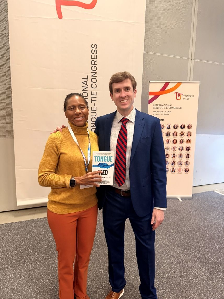Two people smiling and holding an award booklet at a conference booth.