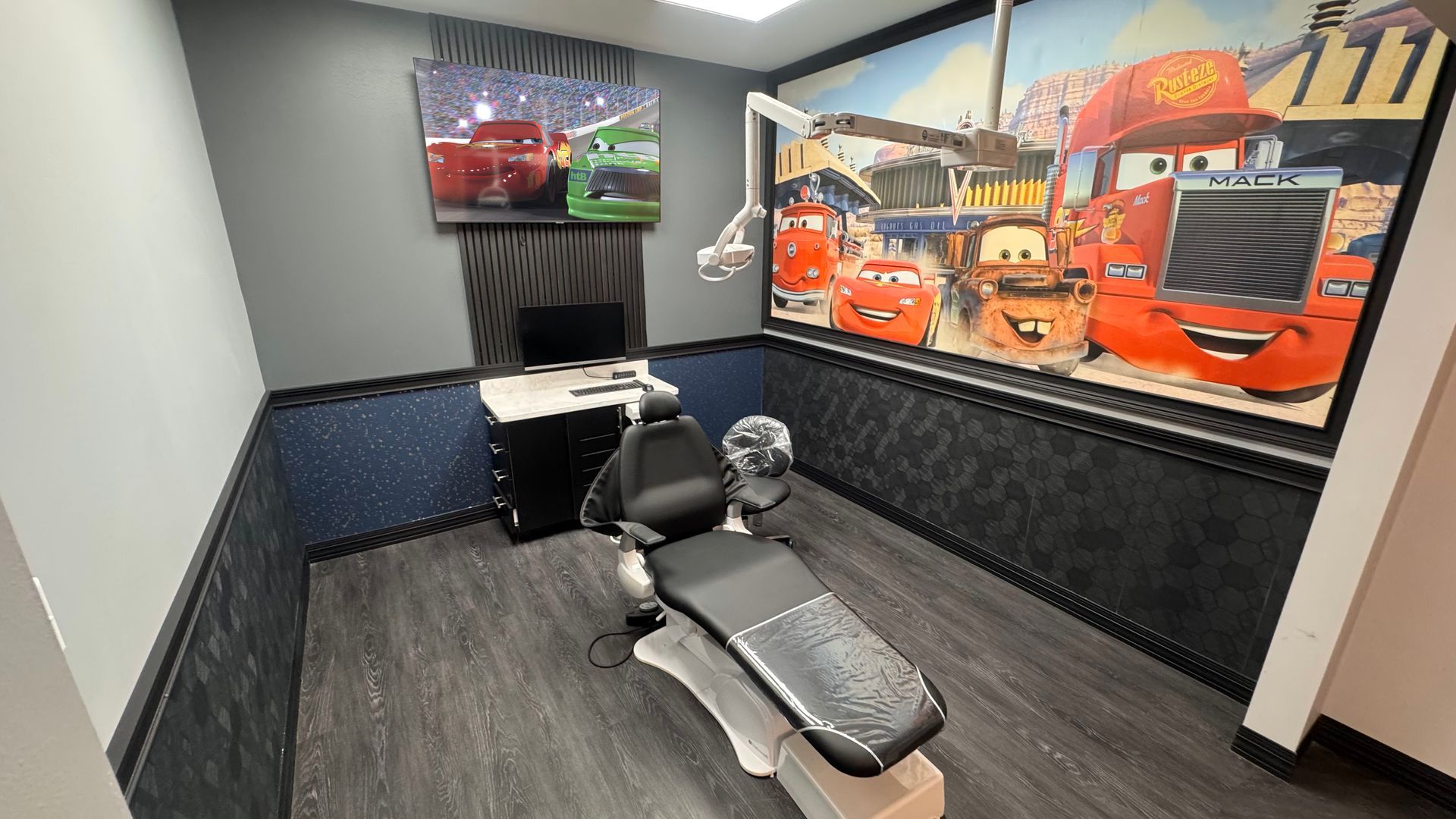 Small office with a dental chair, TV, and large orange truck wall mural.
