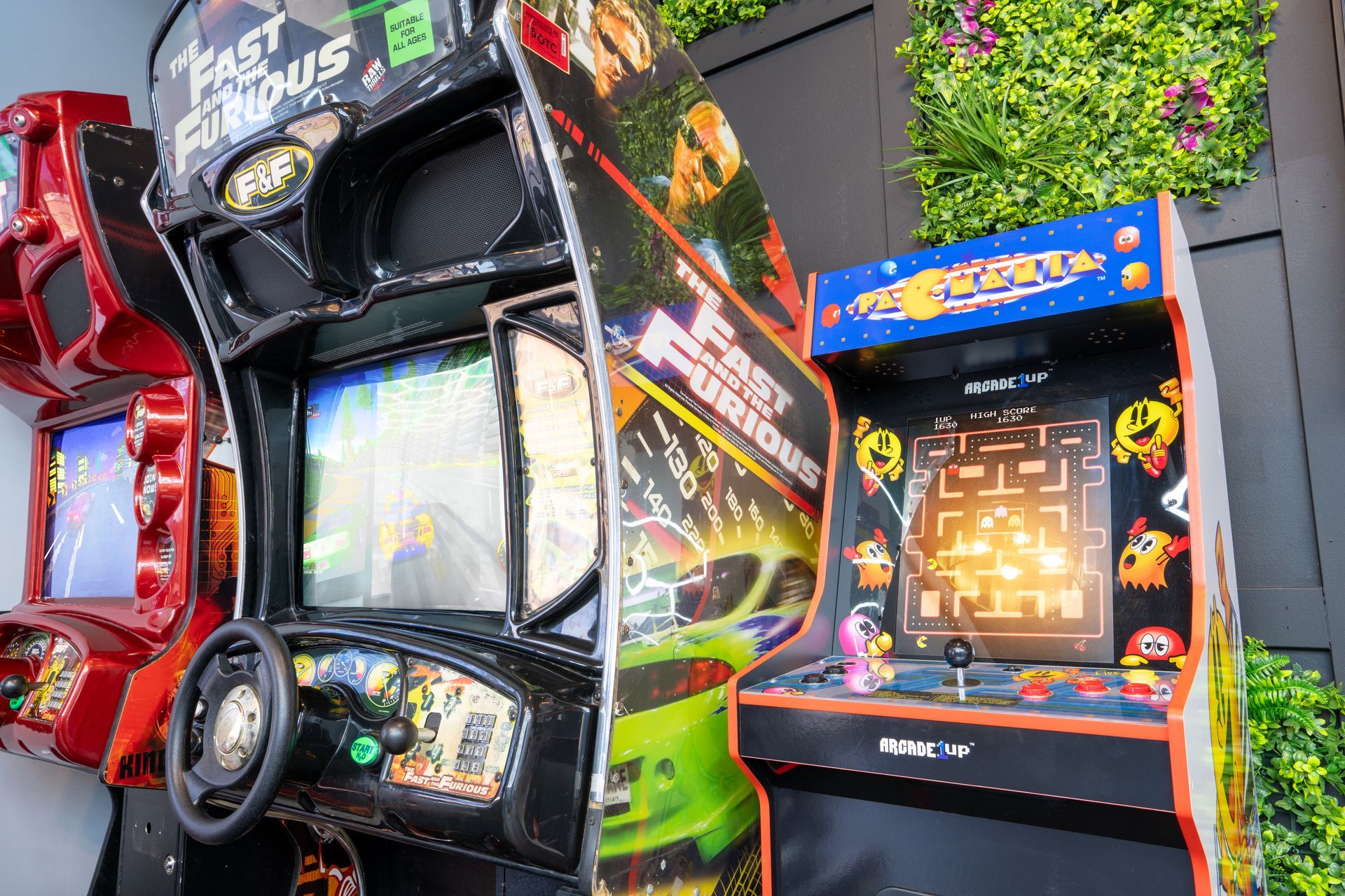 Colorful arcade racing game cabinets lined up indoors, including a Fast & Furious machine and a Pac-Man arcade cabinet