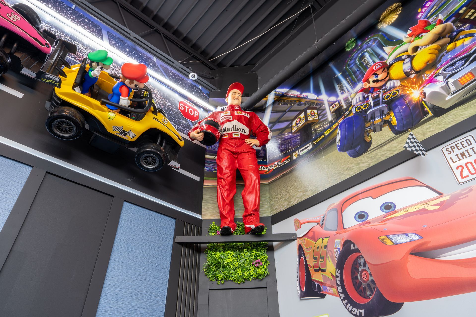 Life-size race car display with a red-clad figure and Lightning McQueen mural in a themed room