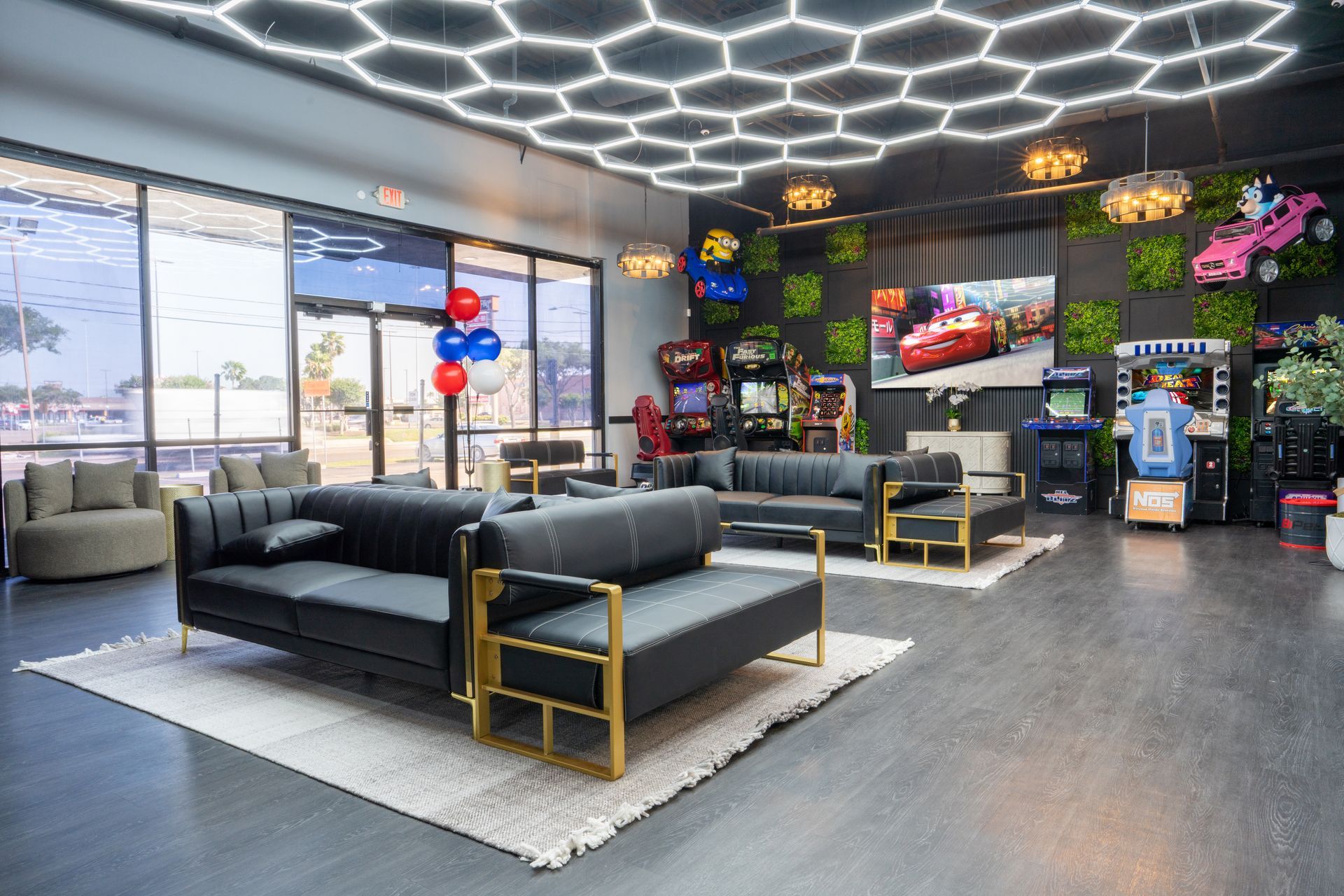 Modern office lounge with black sofas, hexagon ceiling lights, TV, and floor-to-ceiling windows