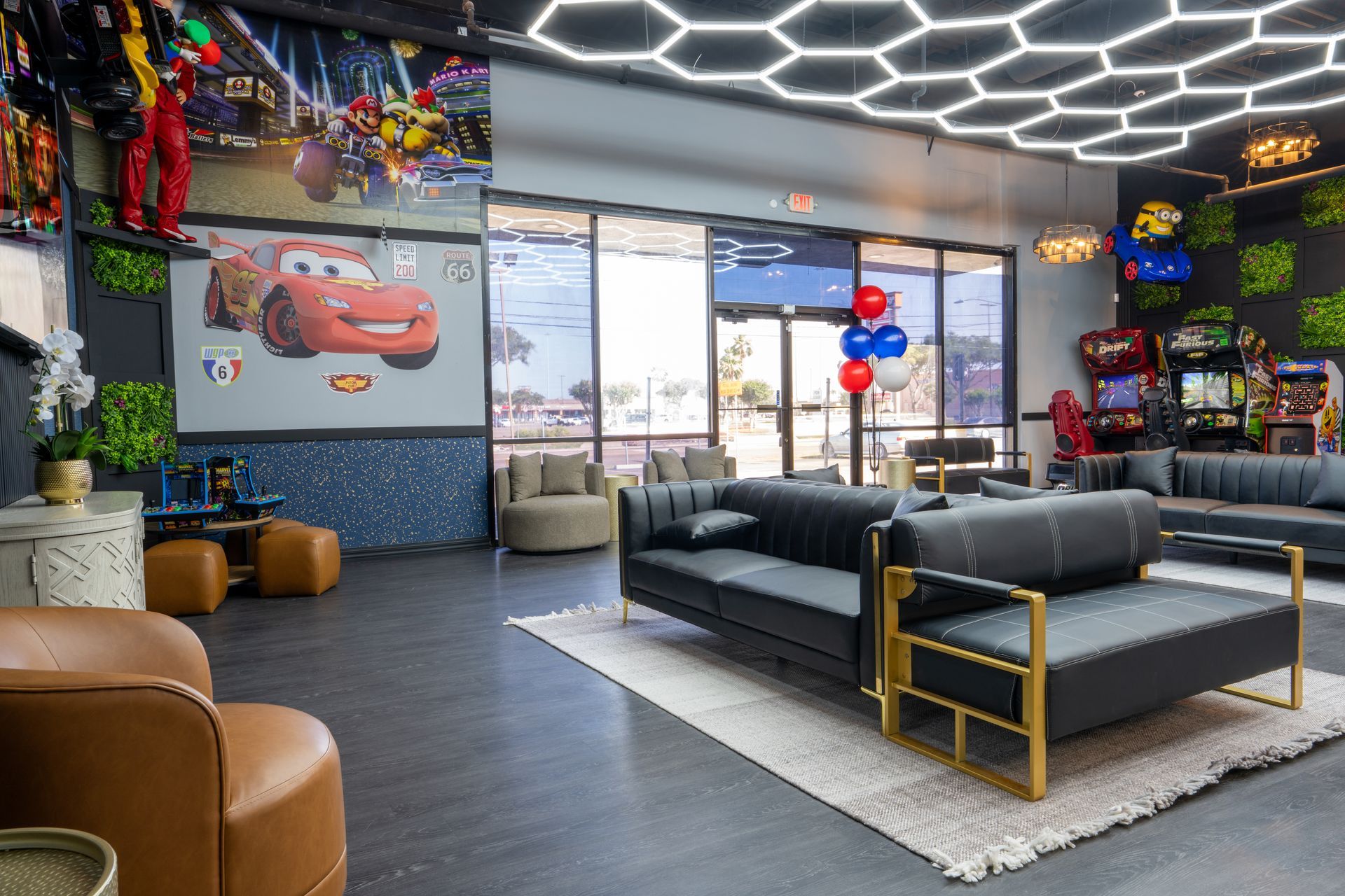 Modern lounge with black sofas, hexagon ceiling lights, balloons, and a wall art of a red sports car.
