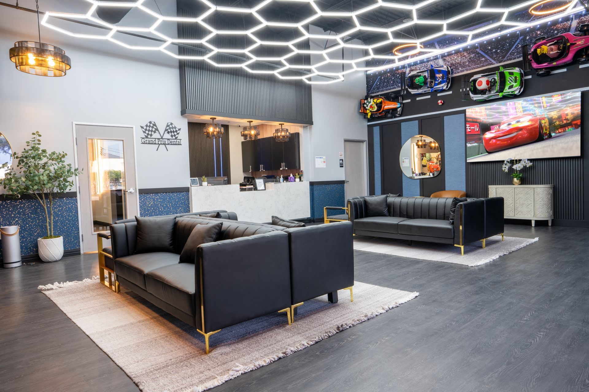 Modern lounge with black sofas, hexagonal ceiling lights, and a large wall-mounted TV.