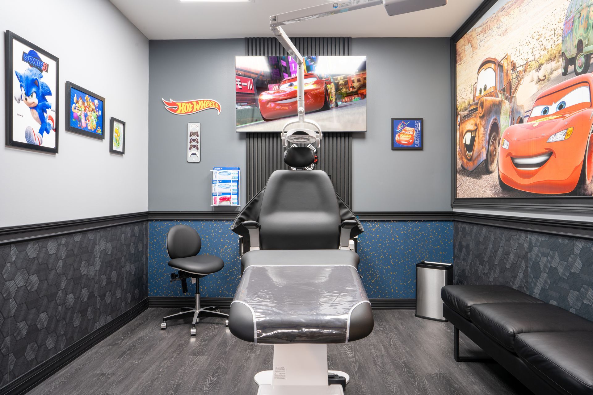 Barber shop interior with a chair, TV screens, Cars wall art, and a black leather waiting bench.