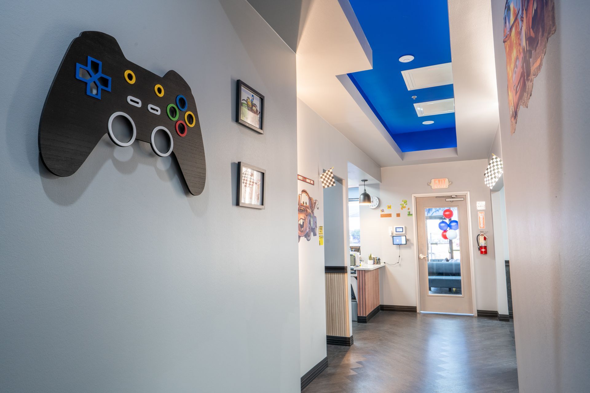 Hallway with a large game controller wall decoration, framed art, and blue accent lights on the ceiling.