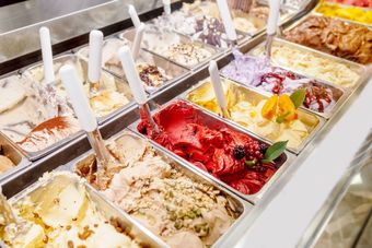Une vitrine remplie de rangées de glaces colorées dans des récipients métalliques, chacun accompagné d'une cuillère de service.