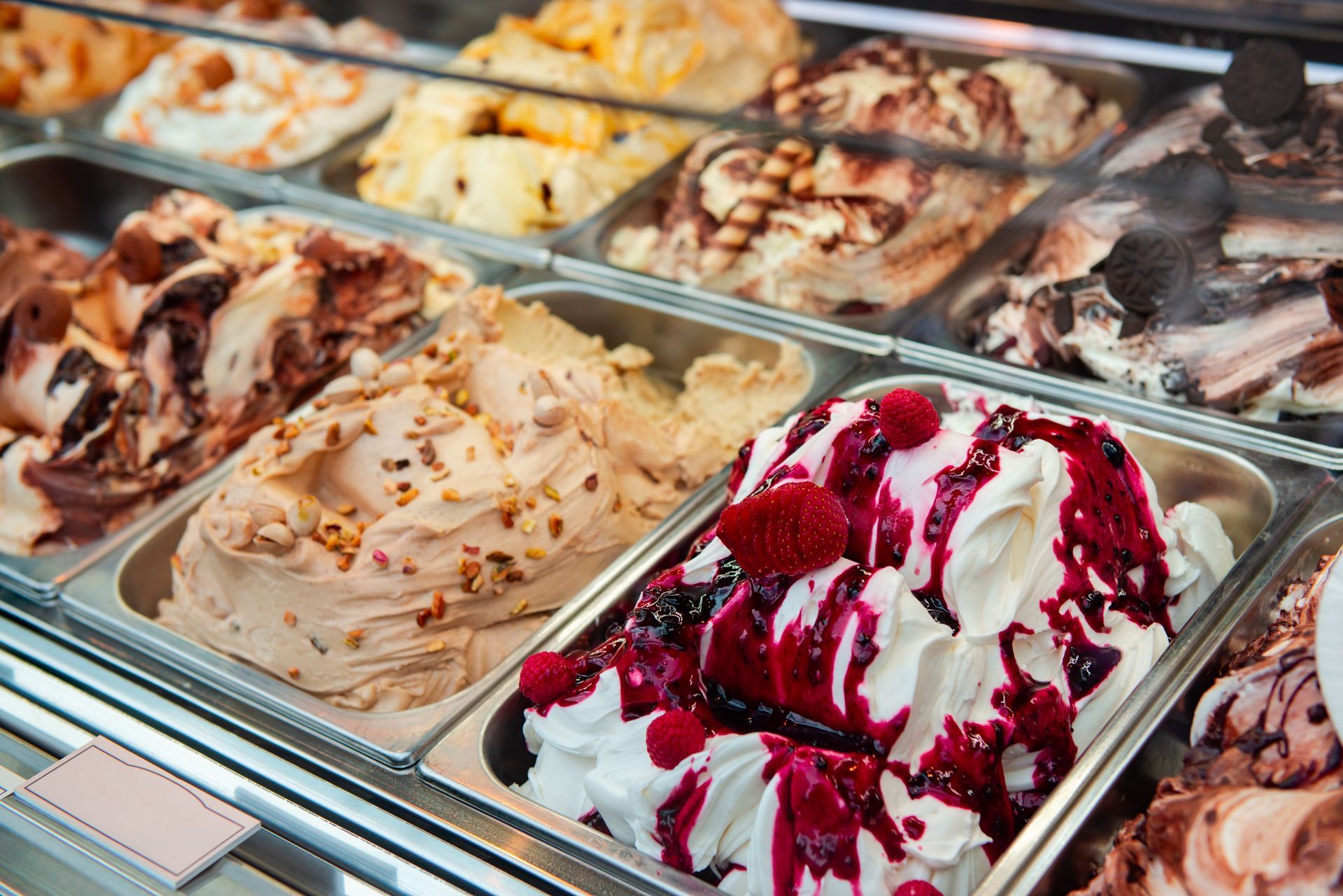Une vitrine remplie de rangées de glaces aux parfums variés, notamment aux fruits rouges, au chocolat et au caramel.