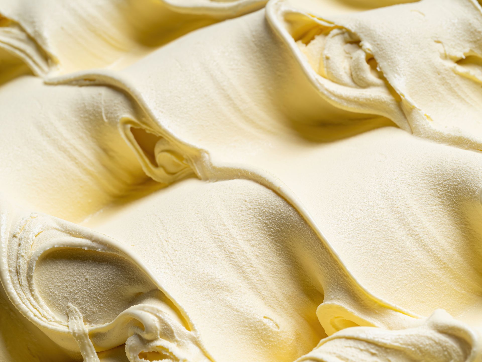 Gros plan sur une glace ou un gelato onctueux, jaune clair, avec des boules et des tourbillons décoratifs.