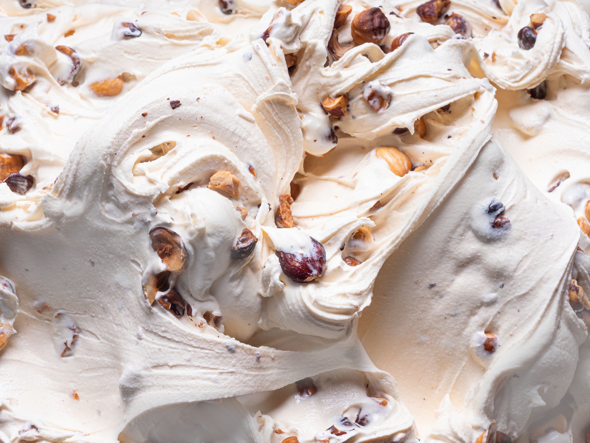 Gros plan sur une glace italienne crémeuse, blanc cassé, agrémentée de morceaux de noix hachées et de pépites de chocolat noir.