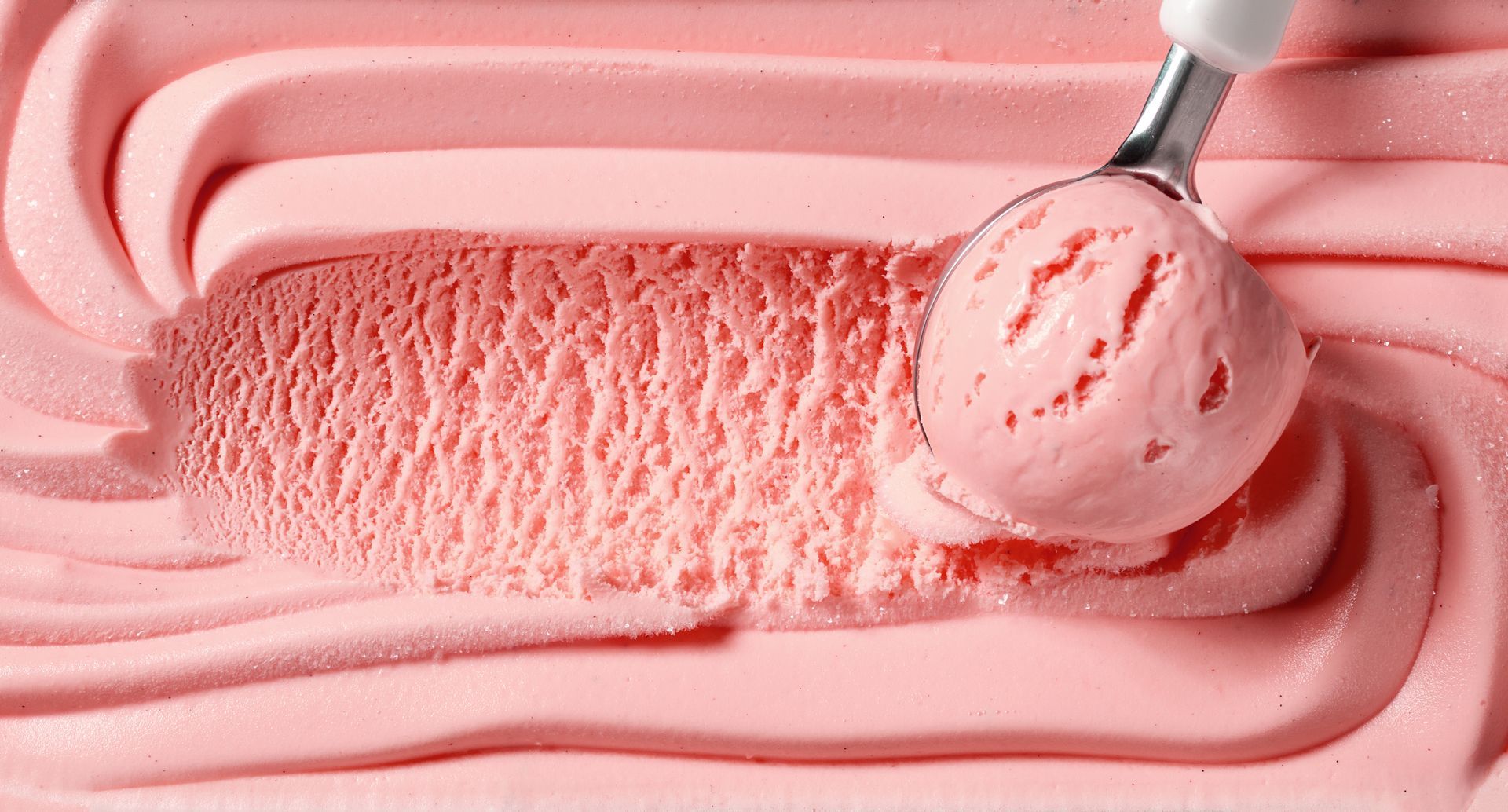 Pink ice cream being scooped with a metal scoop in a close-up tray.
