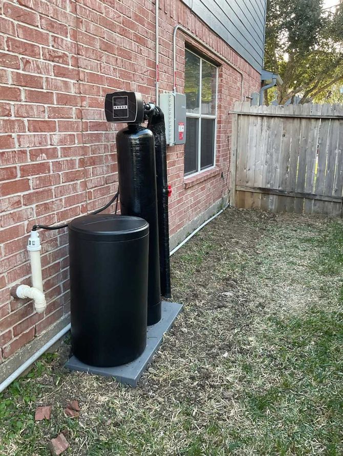 Black water softener system beside a brick house near a window and wooden fence
