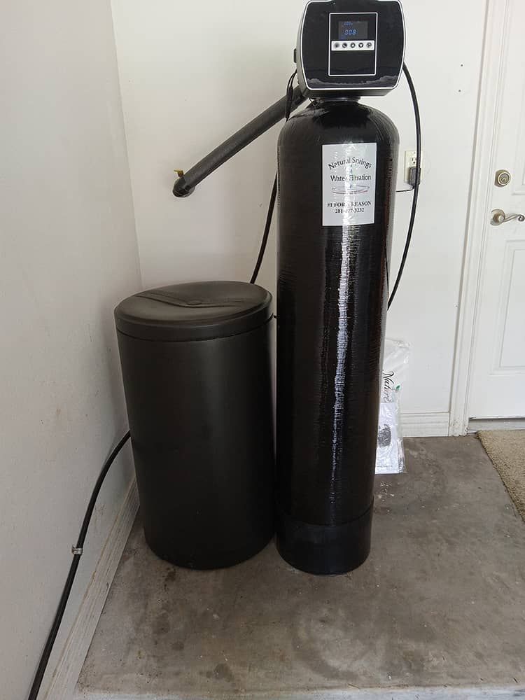 Water softener system with black tank and control unit beside a matching brine tank in a utility room.