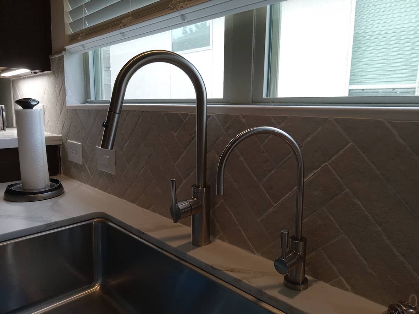 Kitchen sink with two chrome faucets beneath a window and tiled backsplash