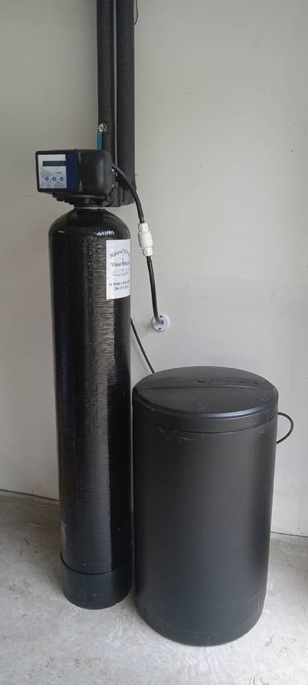 Black water softener system with control head beside a matching brine tank indoors