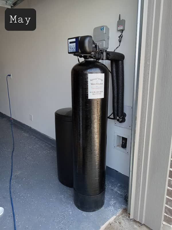 Black cylindrical water treatment tank with control unit beside a wall in a utility room