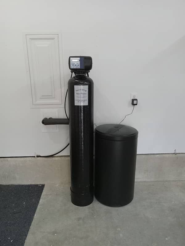 Black water softener system beside a brick house near a window and wooden fence