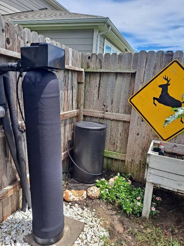 Backyard corner with a black cylindrical tank and a deer crossing sign on a fence