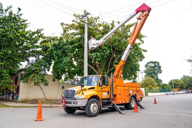 Orange utility truck with raised boom parked on a road beside traffic cones and trees