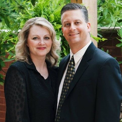 A man in a suit and tie is standing next to a woman in a black shirt.