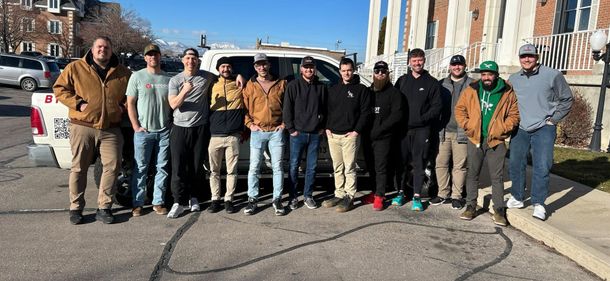 Group of people standing outdoors on a city street in winter, posing in front of parked cars and buildings.