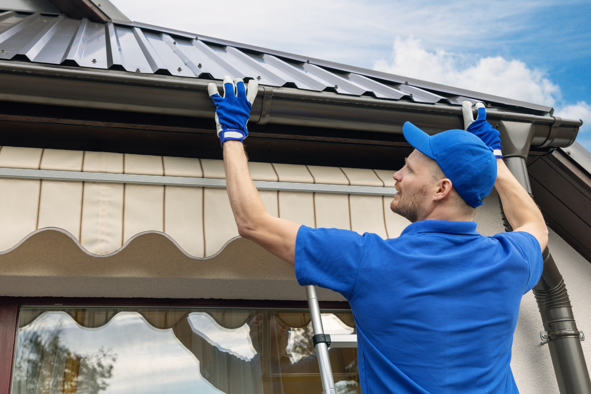 Worker in blue uniform checking a house roof gutter with a gloved hand