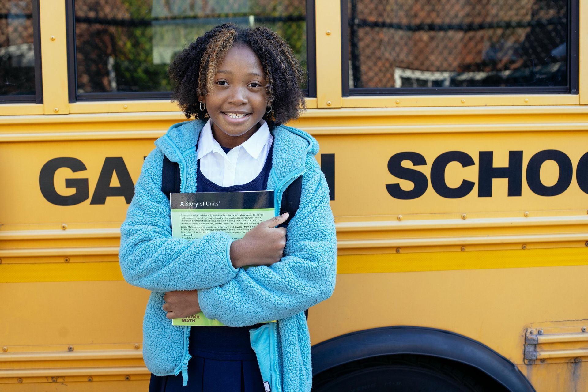 girl standing in front of school bus holding notebook