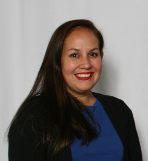 Roxanna with long brown hair smiling, wearing a blue top and black cardigan, against a white backdrop.