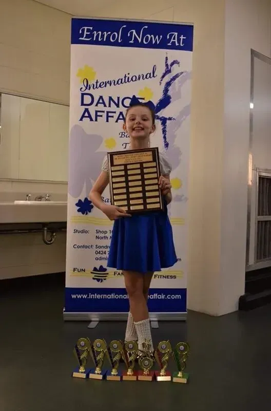 A Girl Holding A Plaque In Front Of A Sign — International Dance Affair In North Mackay, QLD