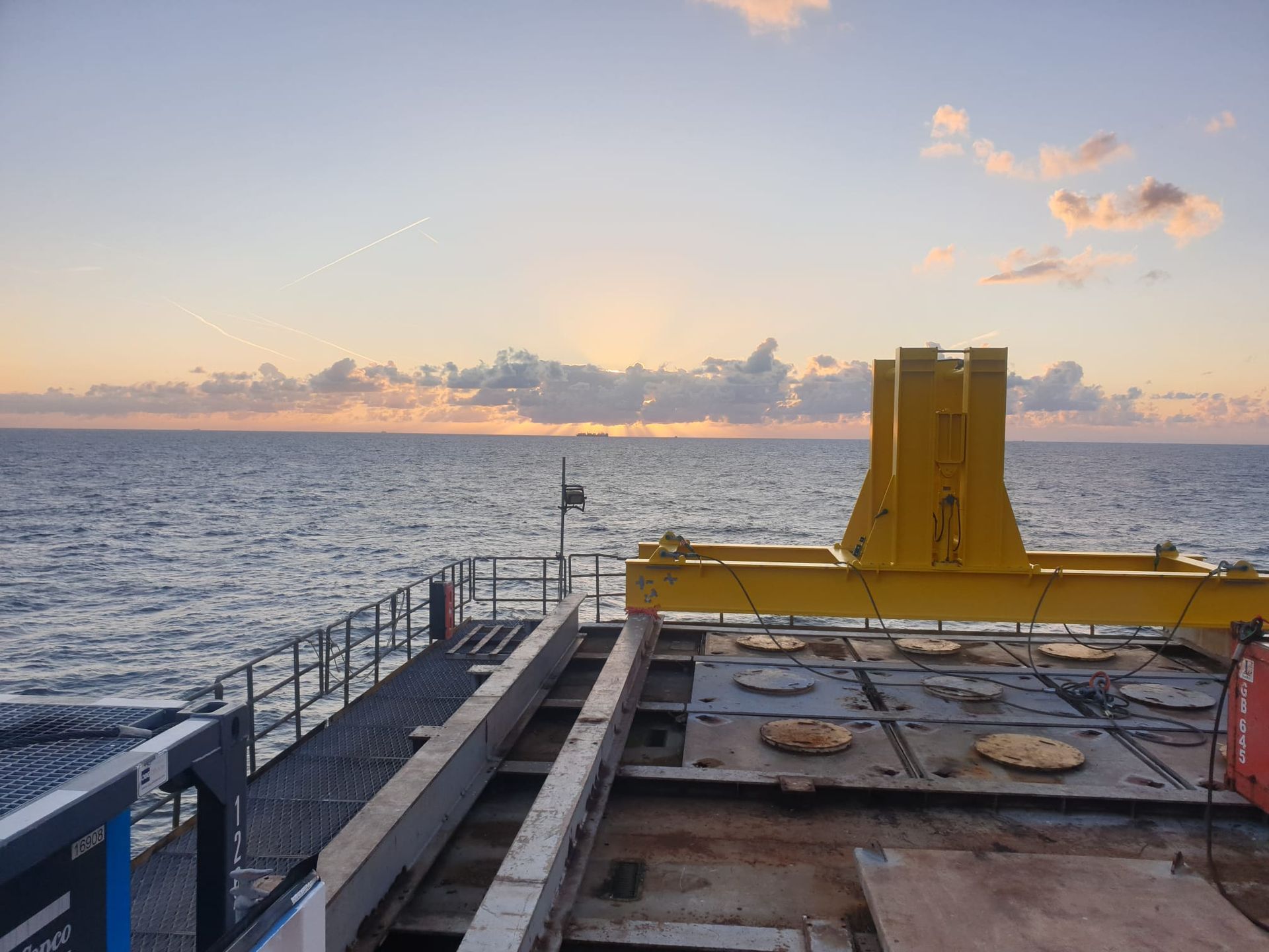 View from a ship at sea with yellow crane, looking towards the sunset.
