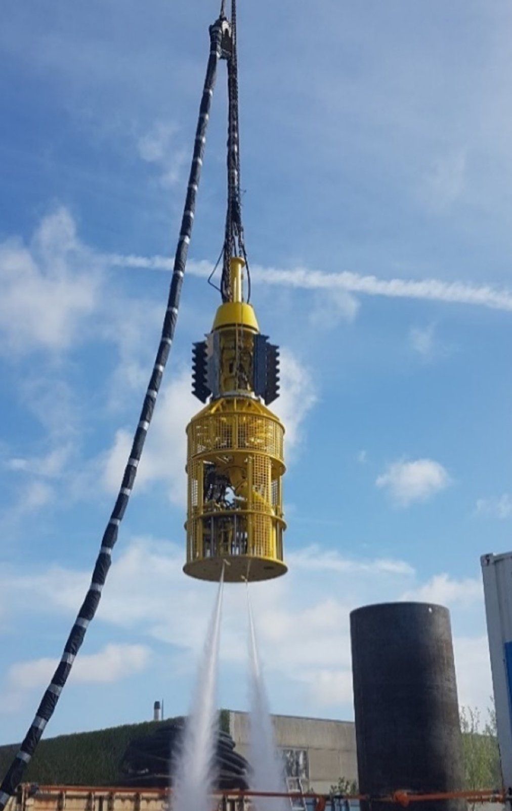 Yellow underwater tool being lowered into the water, spraying water from below against a blue sky.