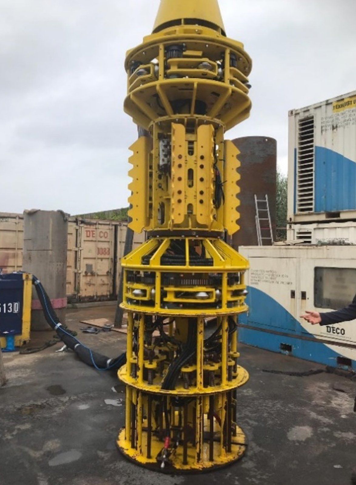 Yellow cylindrical industrial equipment, likely offshore, with a black hose connected.