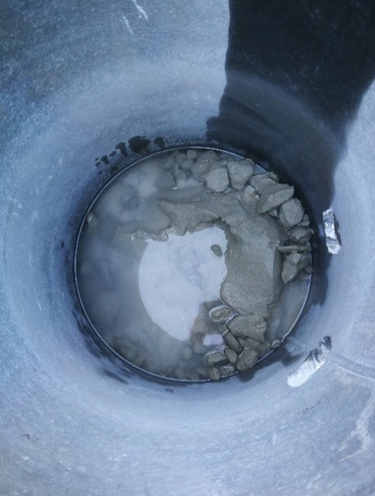 Looking down into a dark bucket filled with water, gravel, and mud.