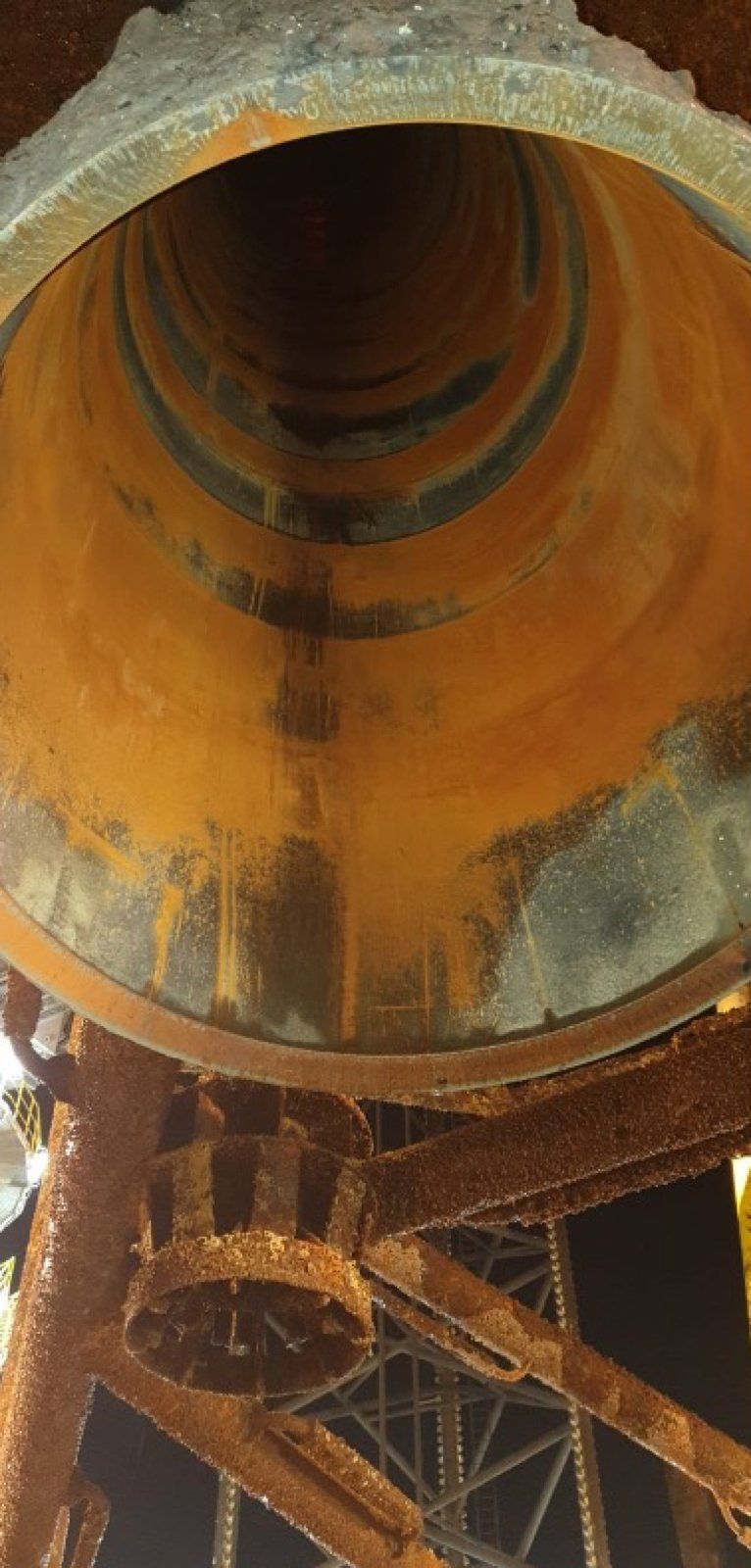 Inside view of a rusty, cylindrical metal structure with dark interior, supported by a framework.