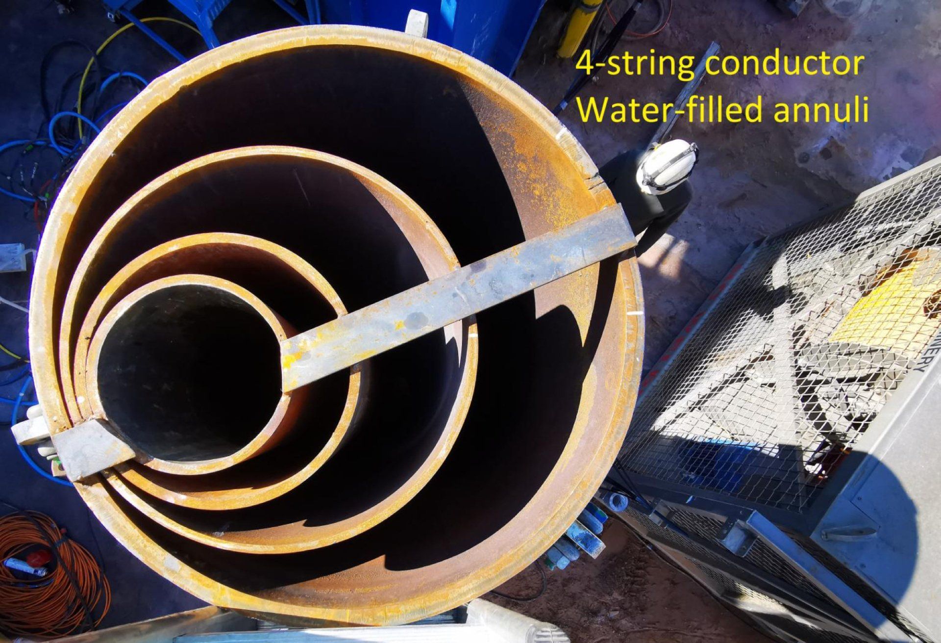 Cross-section of 4-string conductor with water-filled annuli. Rusty metal tubes nested within each other, a worker's head is visible.