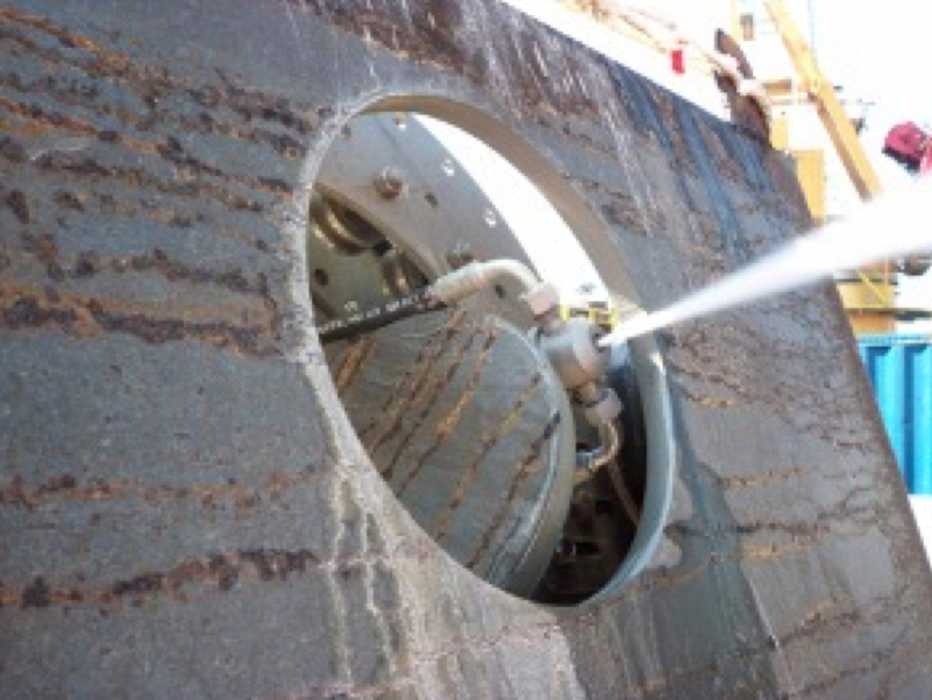 High-pressure water jet cleaning a metal component through a large circular opening.