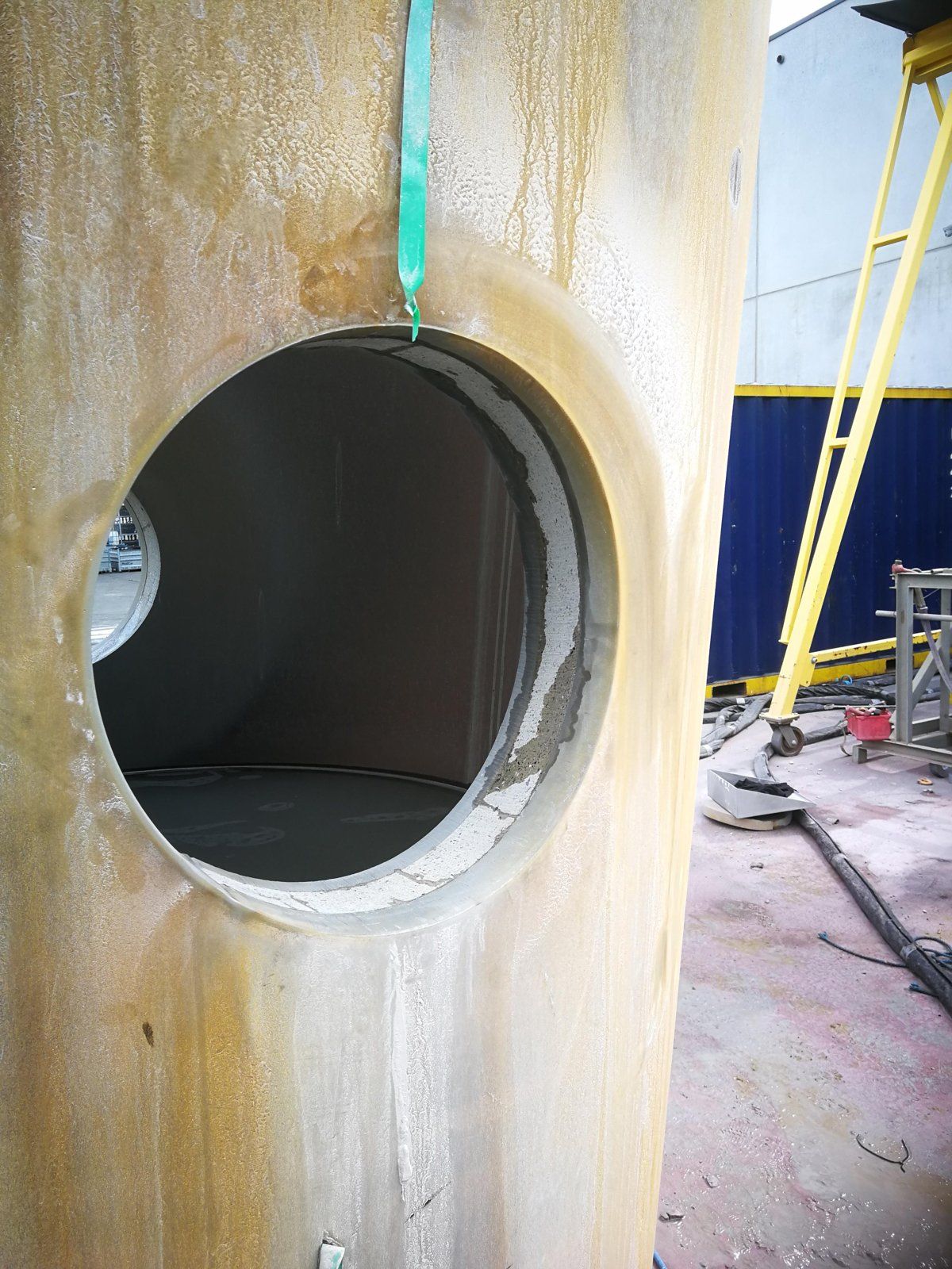 Large cylindrical structure with a circular opening. Inside is gray, outside is tan. A strap is attached.