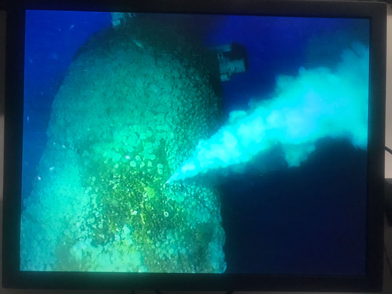 Underwater view of a geyser-like vent emitting cloudy, light blue water.