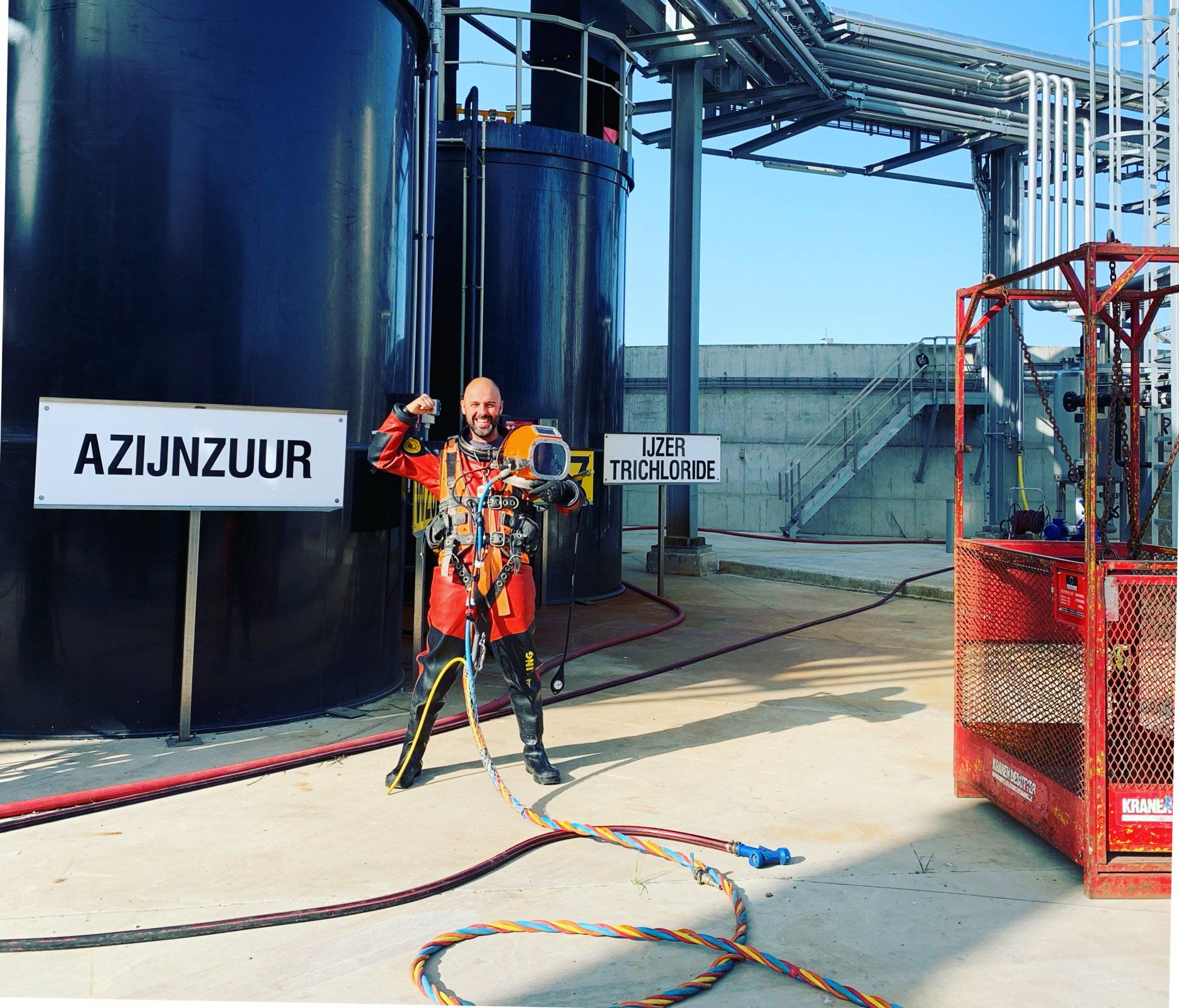 Man in safety gear poses near industrial tank labeled 