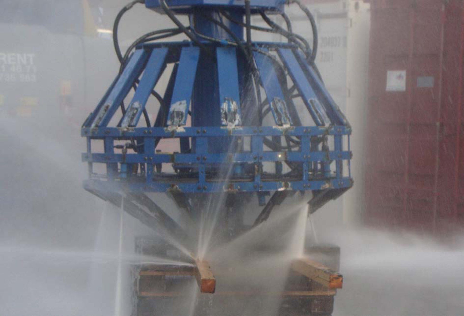 Blue industrial machine spraying water on wooden beams.