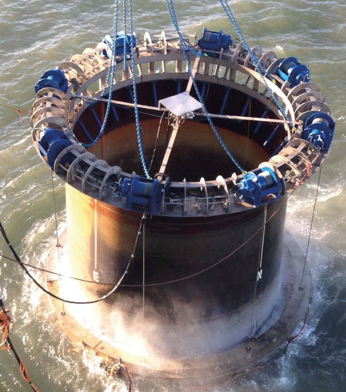 Large cylindrical structure in water being lifted by a crane; white mist rises from the bottom.